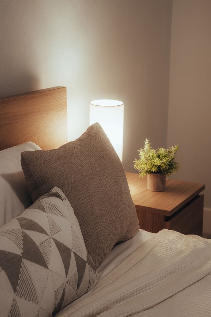 A warm, serene bedroom scene featuring a neatly arranged bed, lamp, and nightstand.