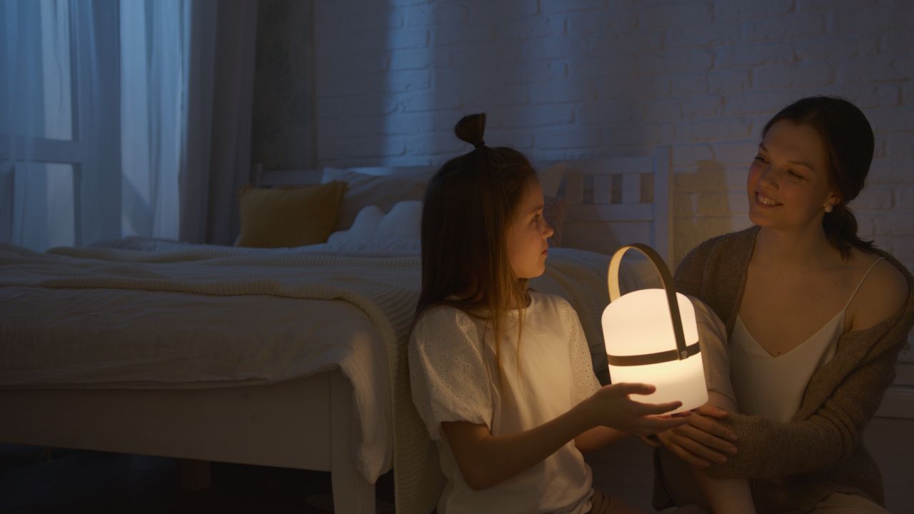A mother and her daughter sharing a warm and intimate moment with a glowing lamp in a cozy bedroom.
