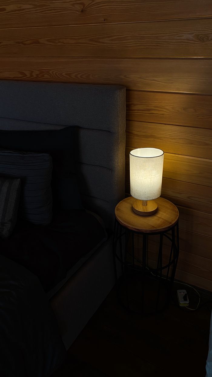 High angle interior of dark room with bed and lamp illuminating on wooden bedside table